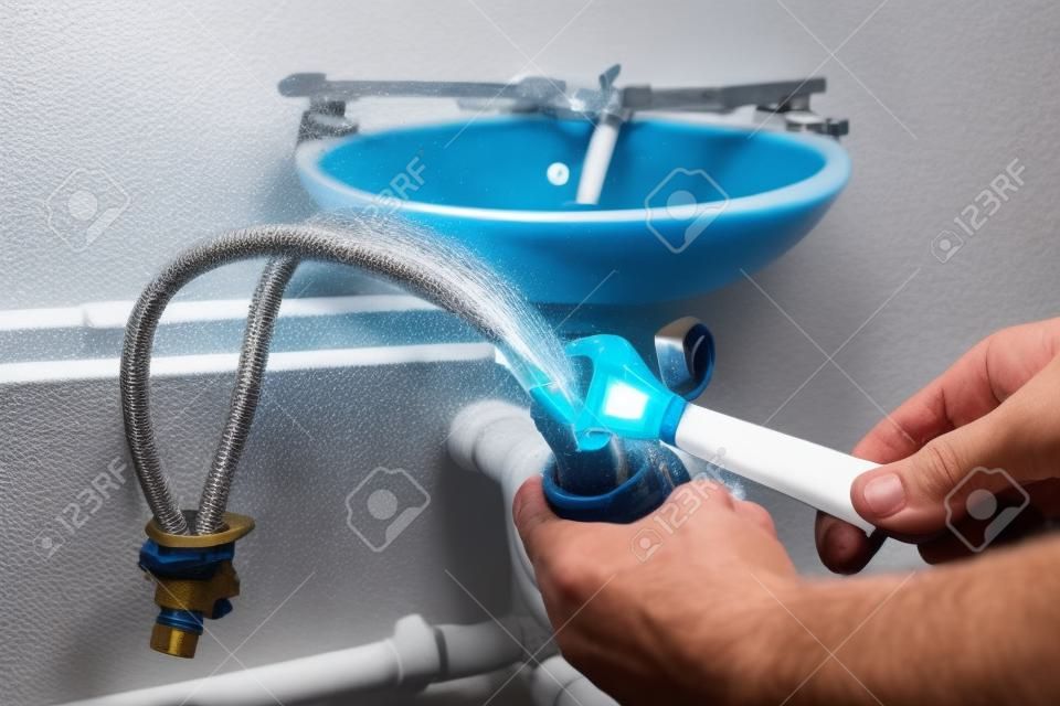 Der Klempner befestigt den geflochtenen Verbindungsschlauch am Wasserhahn, bevor er den Wasserhahn am Waschbecken installiert.