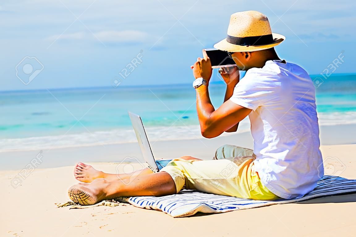 海滩的年轻人与便携式计算机一起使用和在电话里说