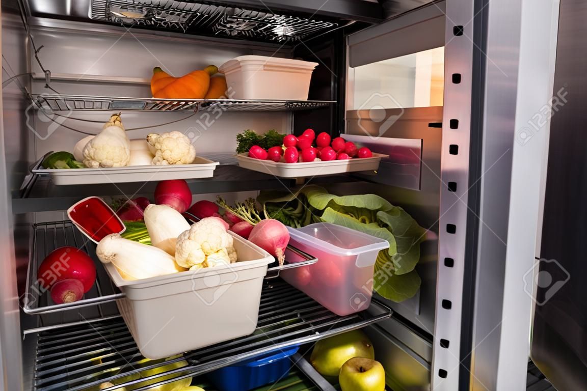 Koelkast van restaurant met voedsel. Groenten in restaurant koelkast. Containers met groenten op de planken van de koelkast. Radijzen, bloemkool en peren in de koelkast camere.