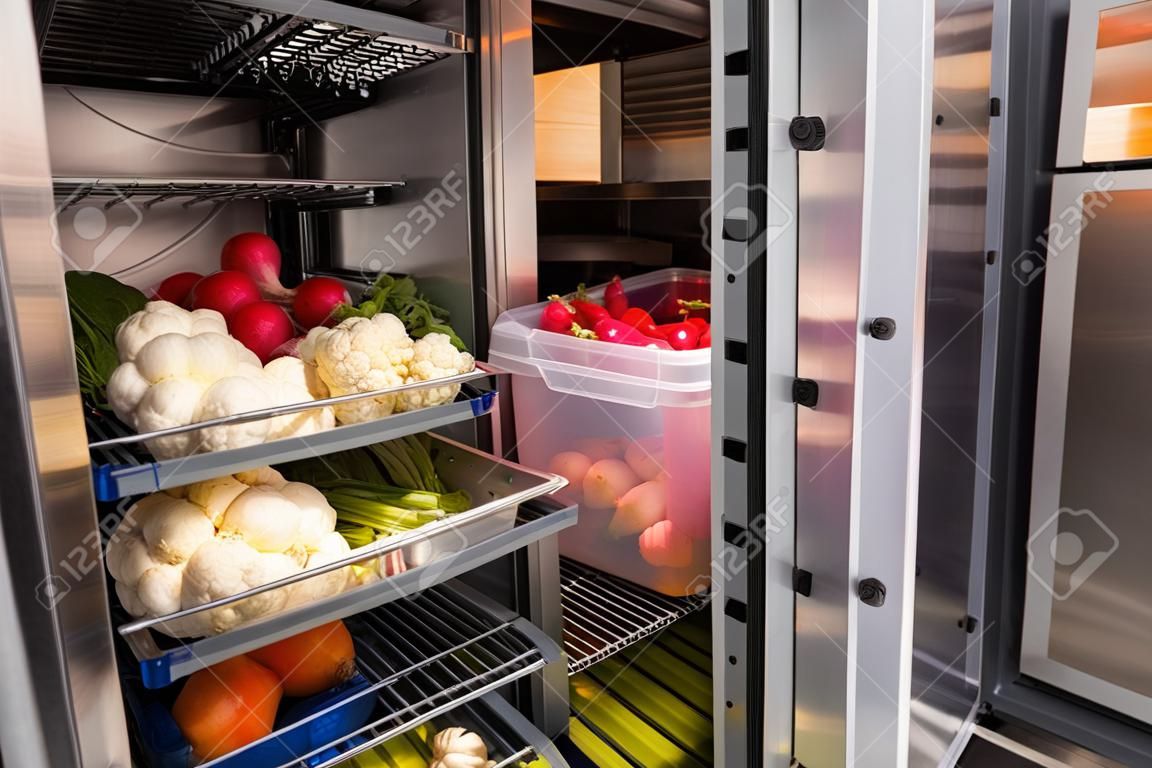 Kühlschrank des Restaurants mit Essen. Gemüse im Kühlschrank des Restaurants. Behälter mit Gemüse in Regalen des Kühlschranks. Radieschen, Blumenkohl und Birnen im Kühlschrank kamere.