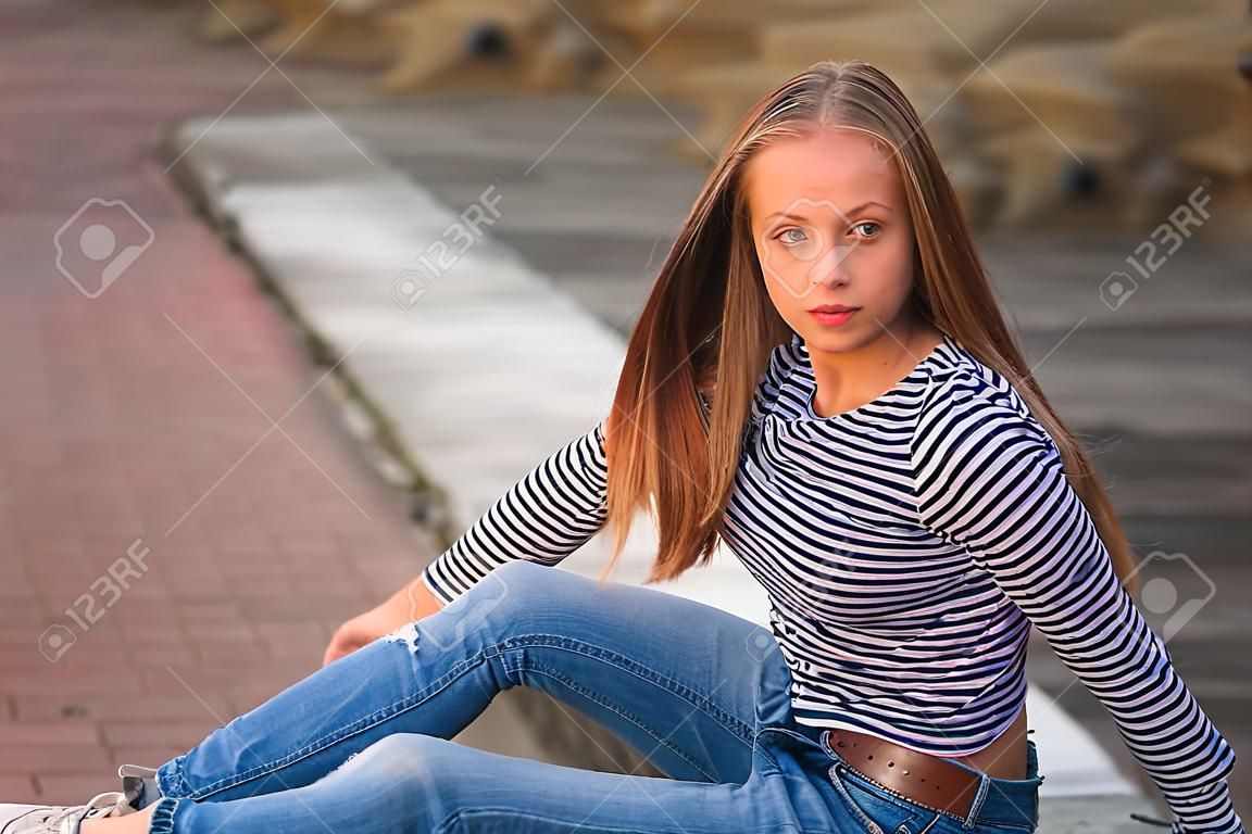 young teenage poses for photo. blonde girl in jeans and blouse. play with hair