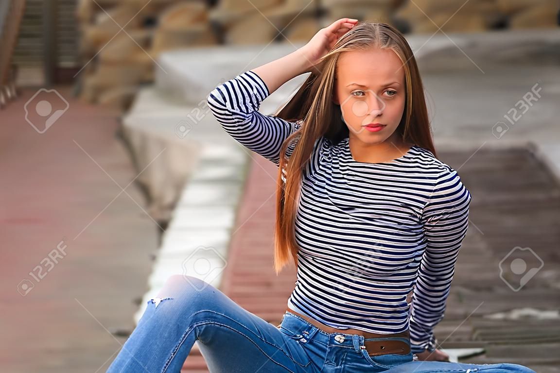 jeune adolescent pose pour la photo. fille blonde en jeans et chemisier. jouer avec les cheveux