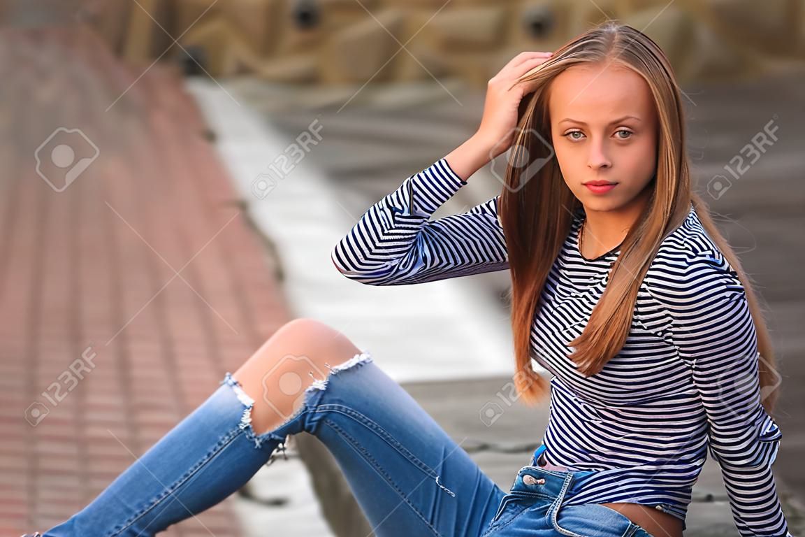 young teenage poses for photo. blonde girl in jeans and blouse. play with hair