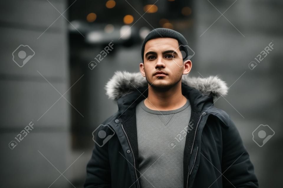 El hombre con una chaqueta gris está parado en la calle y posando para un fotógrafo