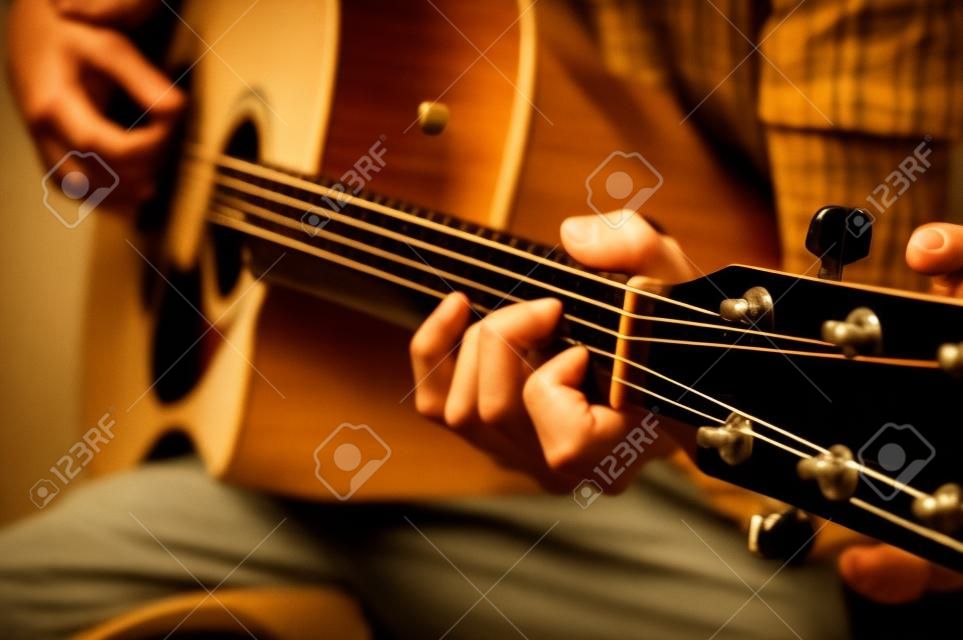 Mężczyzna grający na gitarze akustycznej, pokrywający kursy online, uczący się w domu.