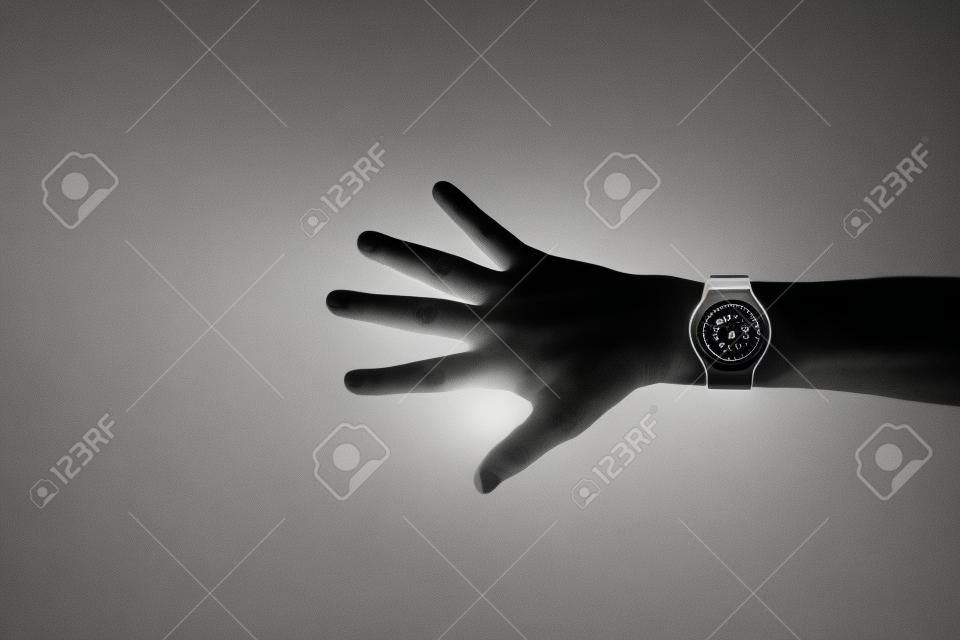 Black and white image of man's hand with smart watch on wrist, displaying blank white screen, isolated on dark background with copy space