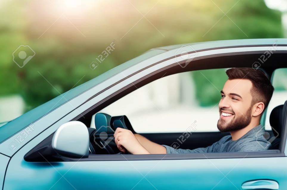 彼の新しい車に乗っています。サイドビューのハンサムな若い男彼の車を運転し、笑みを浮かべて