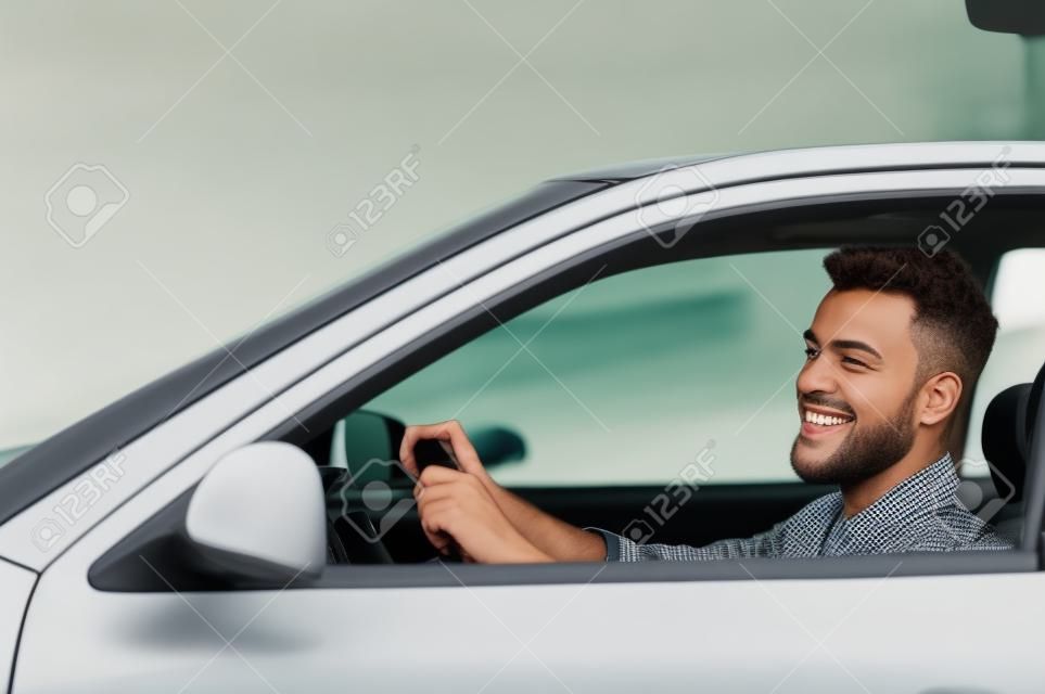 Reitend auf seinem neuen Auto. Seitenansicht der schönen jungen Mann fährt mit seinem Auto und Lächeln