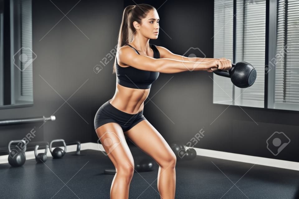 Perfekte Cross-Training. Seitenansicht der jungen schönen Frau mit perfekten Körper in der Sportkleidung arbeitet mit Kesselglocke an der Gymnastik