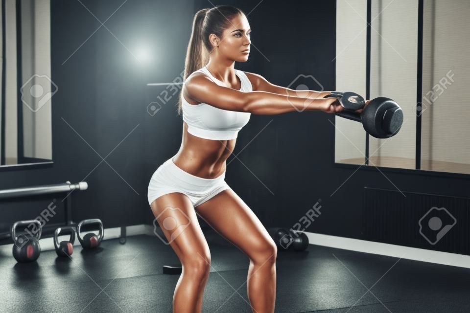 完美的交叉訓練。年輕美麗的女人與運動服完美的身體與健身房的水壺鐘聲工作的側視圖
