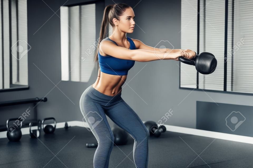 완벽한 크로스 훈련. 스포츠웨어에 완벽한 신체를 가진 젊은 아름 다운 여자의 측면보기 체육관에서 케틀벨을 밖으로 작동