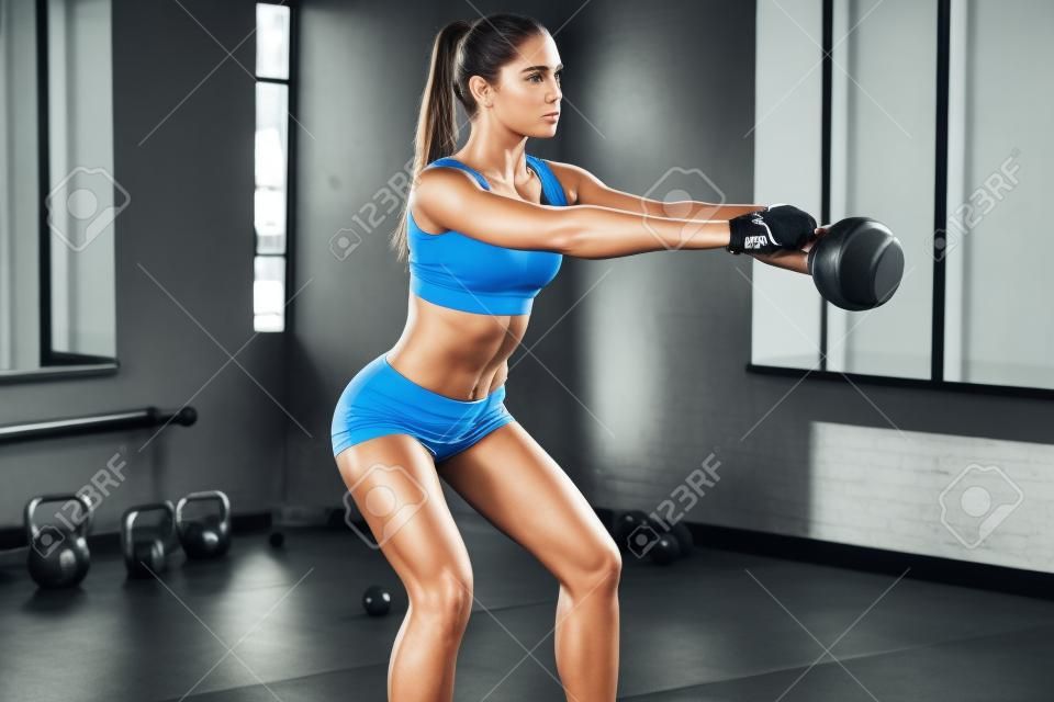 완벽한 크로스 훈련. 스포츠웨어에 완벽한 신체를 가진 젊은 아름 다운 여자의 측면보기 체육관에서 케틀벨을 밖으로 작동