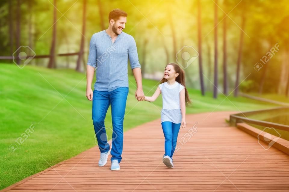 Profitez d'un bon moment avec le père. Vue de face du père joyeux et de la fille tenant les mains et en souriant en marchant dans le parc ensemble