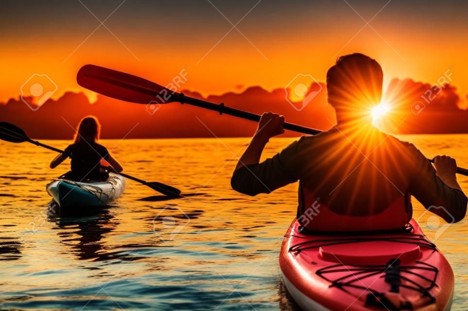 Rencontre de coucher de soleil sur les kayaks. Vue arrière, de, beau jeune couple, kayak, sur, lac, ensemble, à, coucher soleil, dans, les, arrière-plan