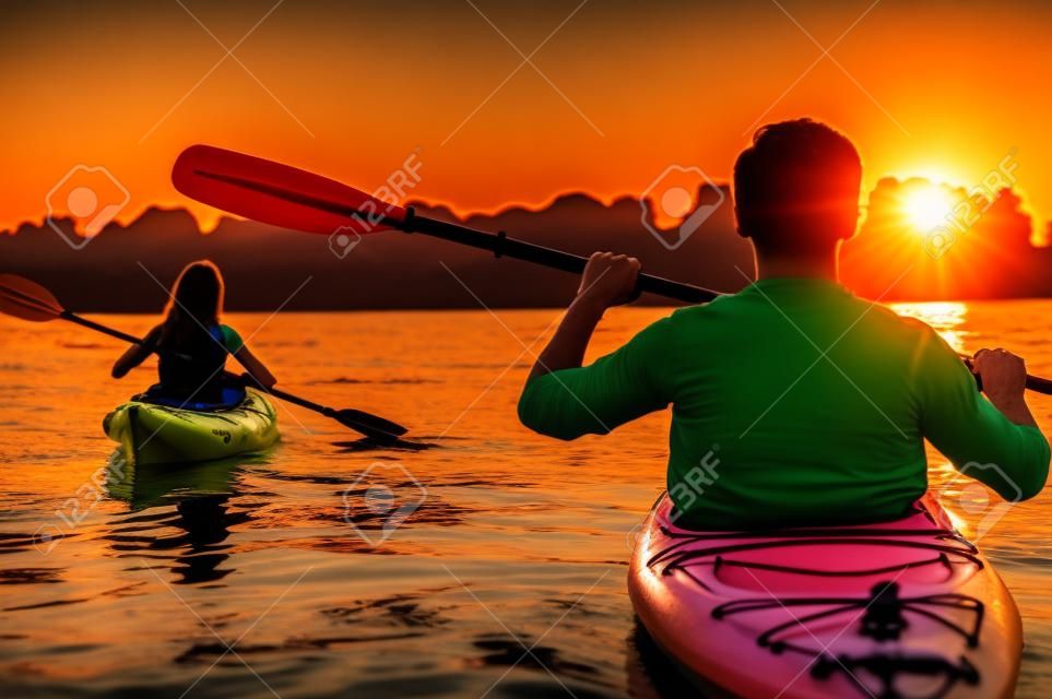 會議在皮划艇上的日落。美麗的年輕夫婦，在日落時分在湖上劃獨木舟的後視圖