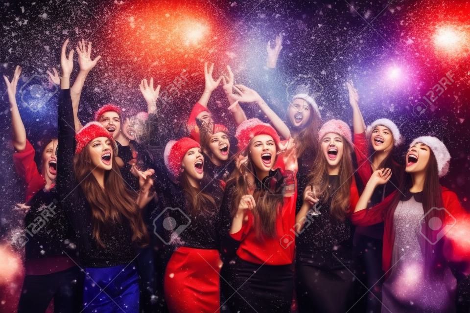 Celebrando o Ano Novo juntos. Grupo de jovens bonitos em chapéus de Papai Noel jogando confete colorido e olhando feliz