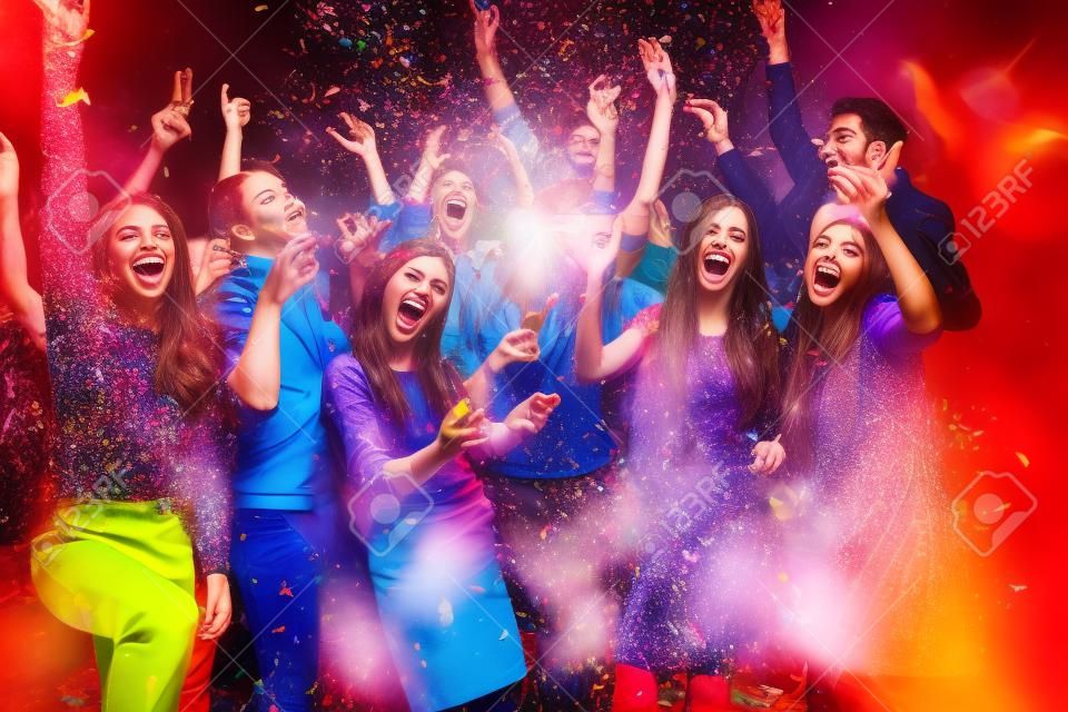 Partia zabawy. Grupa pięknych młodych ludzi rzucających kolorowe konfetti i patrząc szczęśliwy