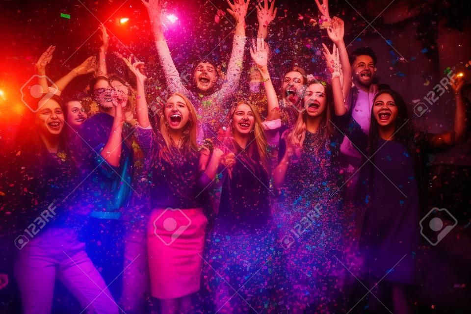 What a night! Group of beautiful young people throwing colorful confetti and looking happy