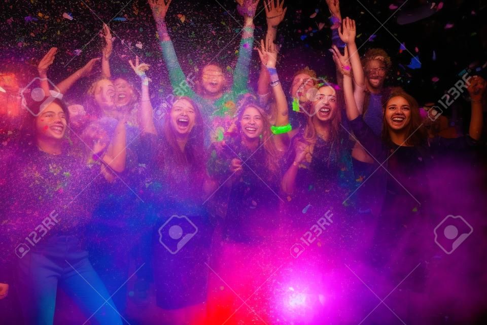 What a night! Group of beautiful young people throwing colorful confetti and looking happy