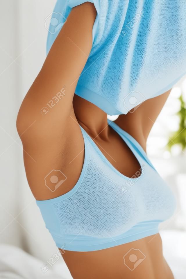 No need to be dressed!  Close-up of young woman in underwear taking off her T-shirt and keeping eyes closed while standing in the bedroom