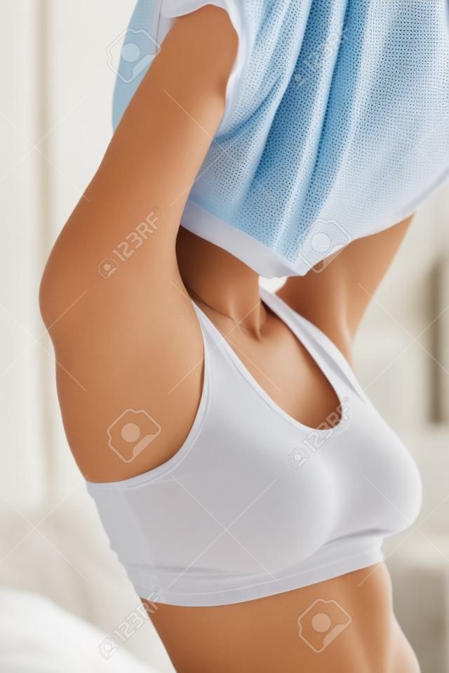 No need to be dressed!  Close-up of young woman in underwear taking off her T-shirt and keeping eyes closed while standing in the bedroom