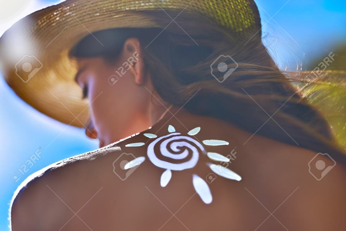 Veilig blijven de hele zomer lang. Lage hoek achteraanzicht van de jonge vrouw met een zonnebrandlotion op haar schouder zonnebaden tijdens het zitten buiten