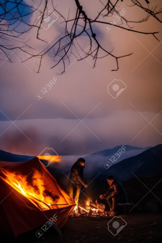 Mooi jong stel dat opwarmt bij het kampvuur tijdens het kamperen in de bergen