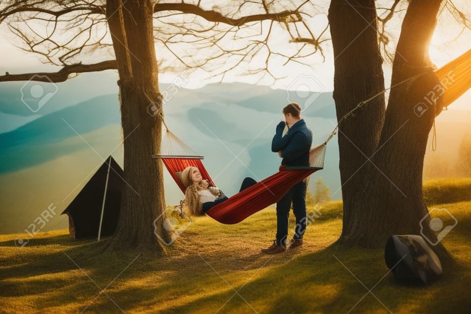 Attractive young woman lying in hammock while her boyfriend standing next to her
