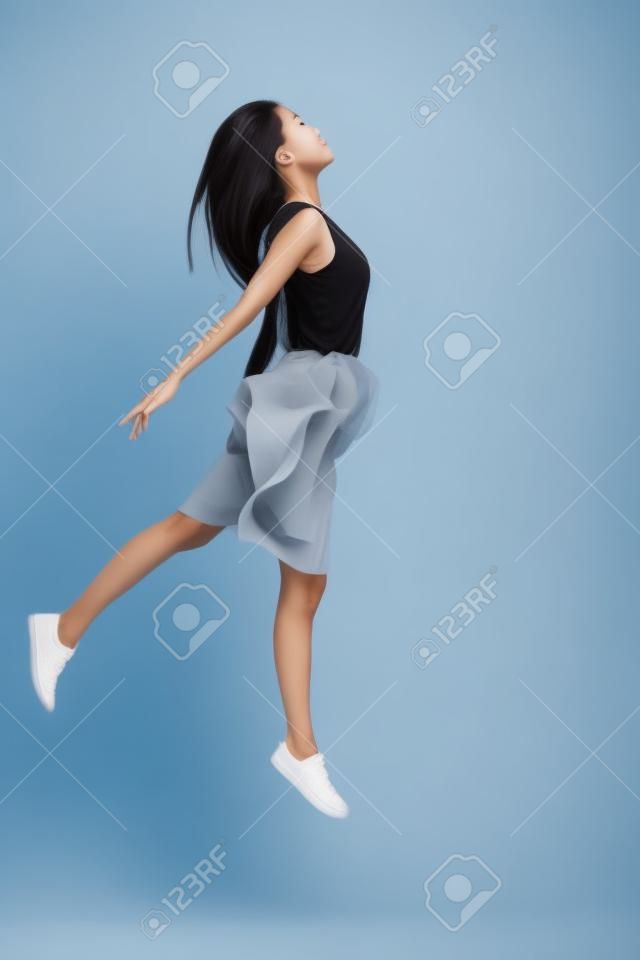 Brak grawitacji. pełna długość pięknej młodej kobiety azjatyckiej unoszącej się na szarym tle