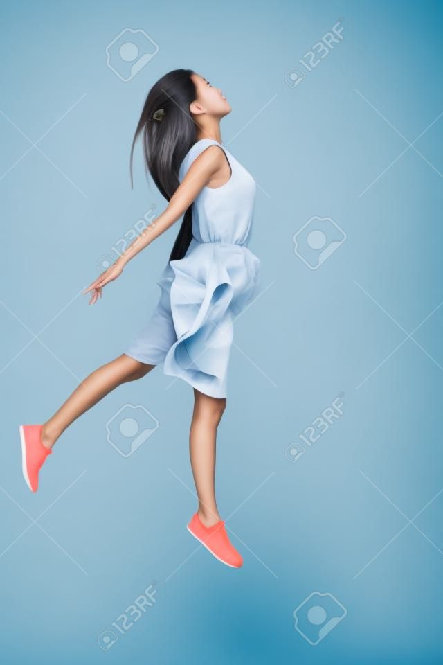 Zero gravity. Full length of beautiful young Asian woman hovering against grey background