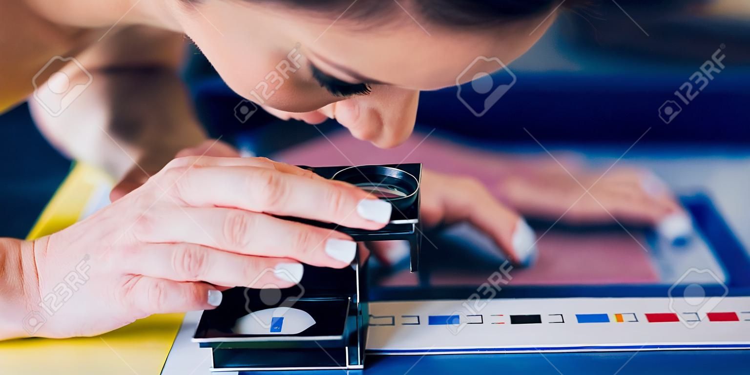 Worker in a printing and press centar uses a magnifying glass and check the print quality