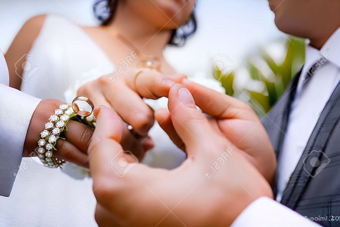 신랑은 신부 손에 결혼 반지를 씌워줍니다. 아름다운 결혼식에는 신선한 꽃과 아름다운 소녀와 용감한 남자가 클로즈업 반지를