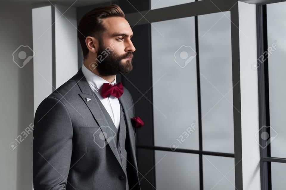 A stately handsome man with a beard dressed in a classic suit and a bow tie