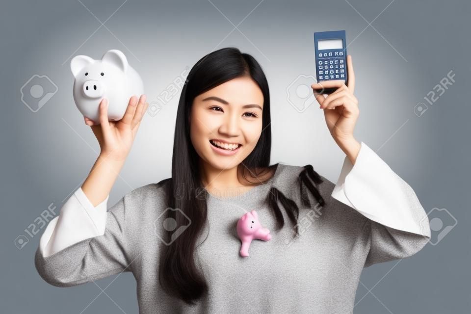 Asian woman with calculator and piggy bank on gray background