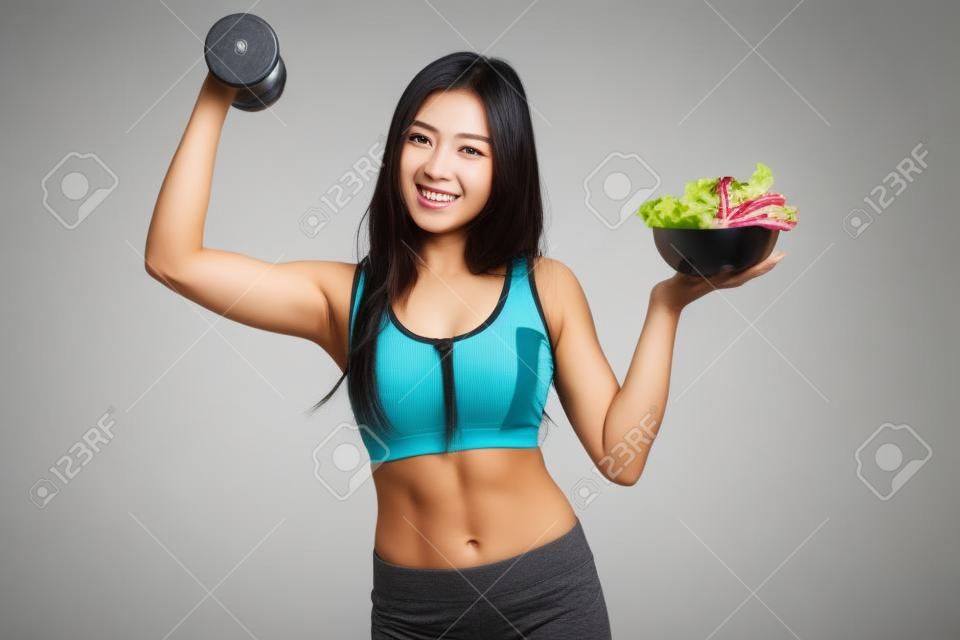 Beautiful Asian healthy girl with dumbbell and salad on white background