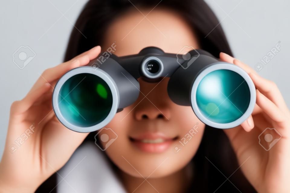 Joven mujer asiática con binoculares sobre fondo blanco.