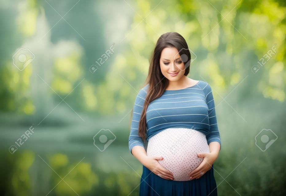 Outdoor portrait of beautiful pregnant woman holding her belly