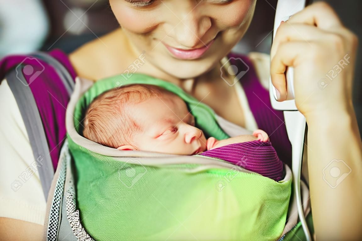 Новорожденный ребенок удерживайте матерью в детской Wrap Перевозчик. Мама призвание на телефон.