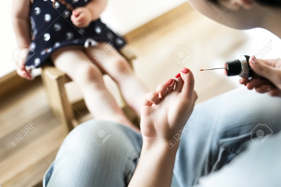 Close up of unrecognizable young father at home painting nails of her cute little daughter.