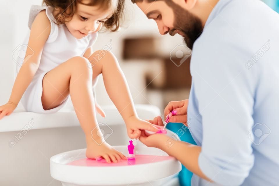 Junger vater malt kleine töchternägel in einem badezimmer zu hause.
