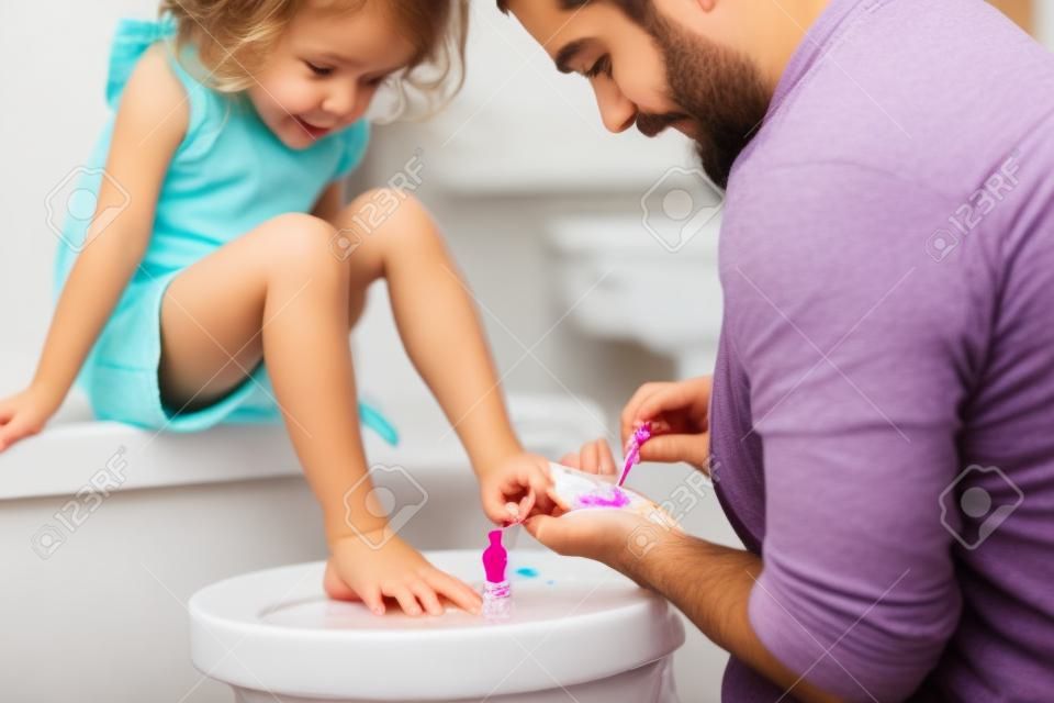 Jonge vader schildert kleine dochters nagels in een badkamer thuis.