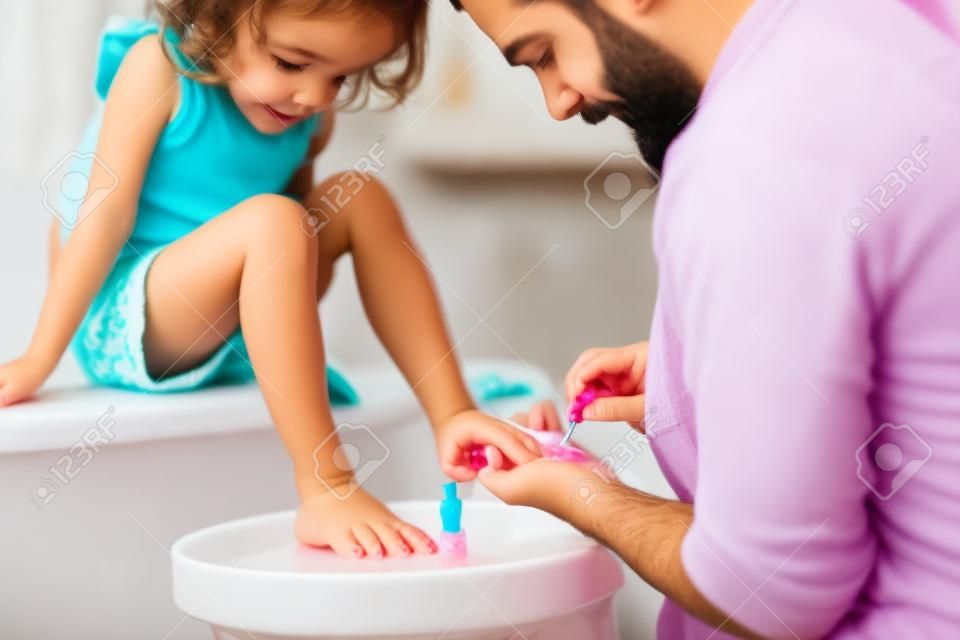 Jeune père peignant des ongles de petites filles dans une salle de bain à la maison.