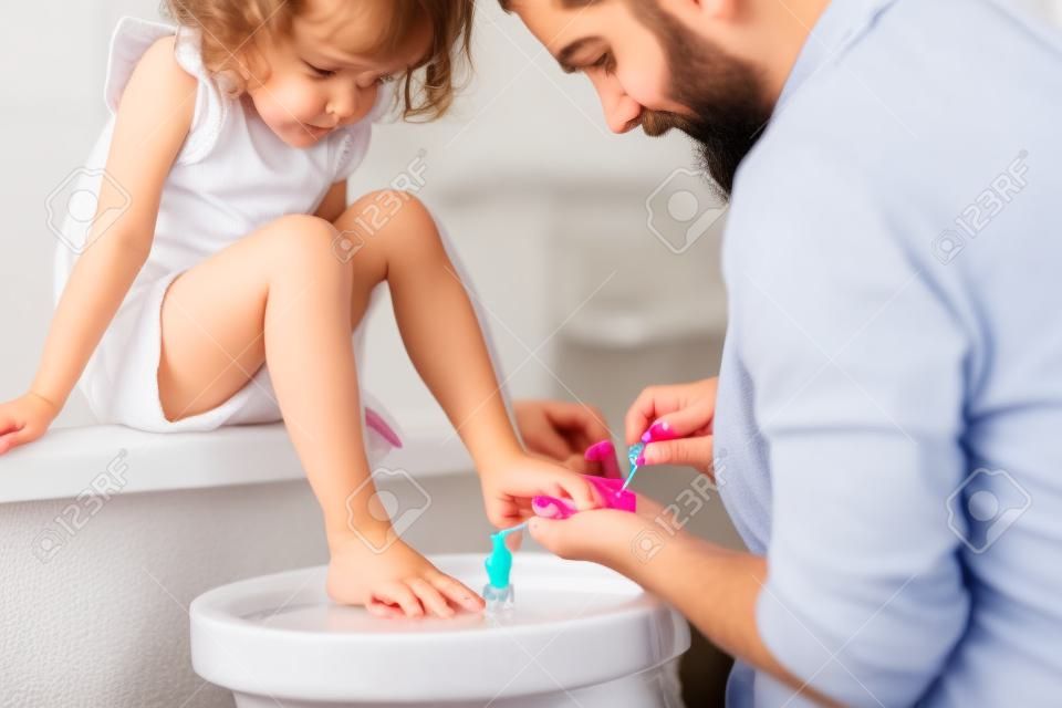 Jeune père peignant des ongles de petites filles dans une salle de bain à la maison.