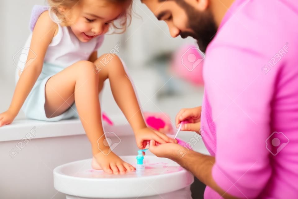 Pai jovem pintando unhas de filhas pequenas em um banheiro em casa.