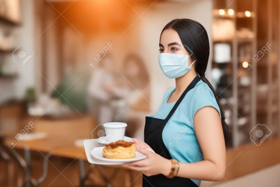 Młoda kobieta z maską pracuje w kawiarni, obsługując klientów.
