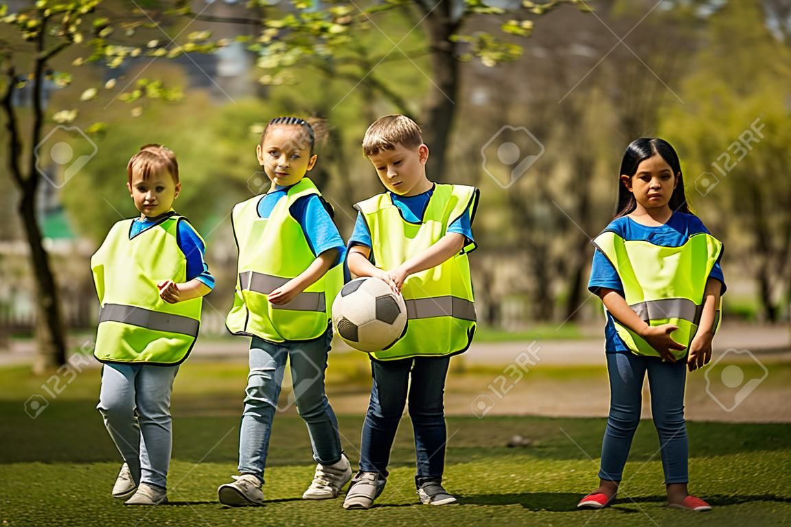 Small children with ball looking at camera outdoors in city park, learning group education concept.
