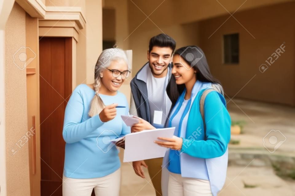 Jóvenes voluntarios puerta a puerta hablando con una anciana y haciendo una encuesta en la puerta de su casa.