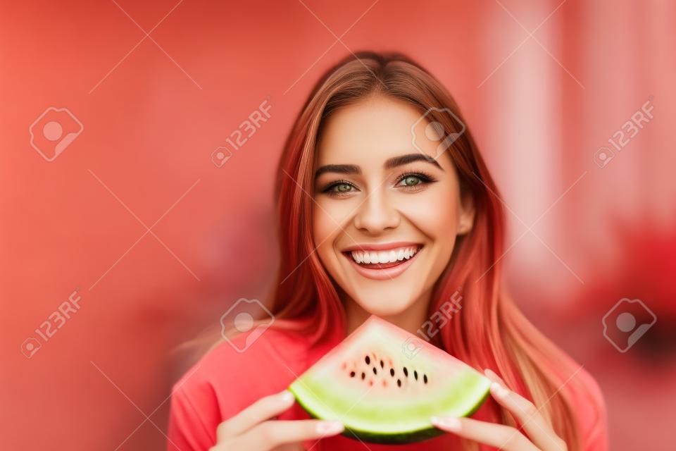 Portret van mooie jonge vrouw die watermeloen eet en naar camera kijkt.