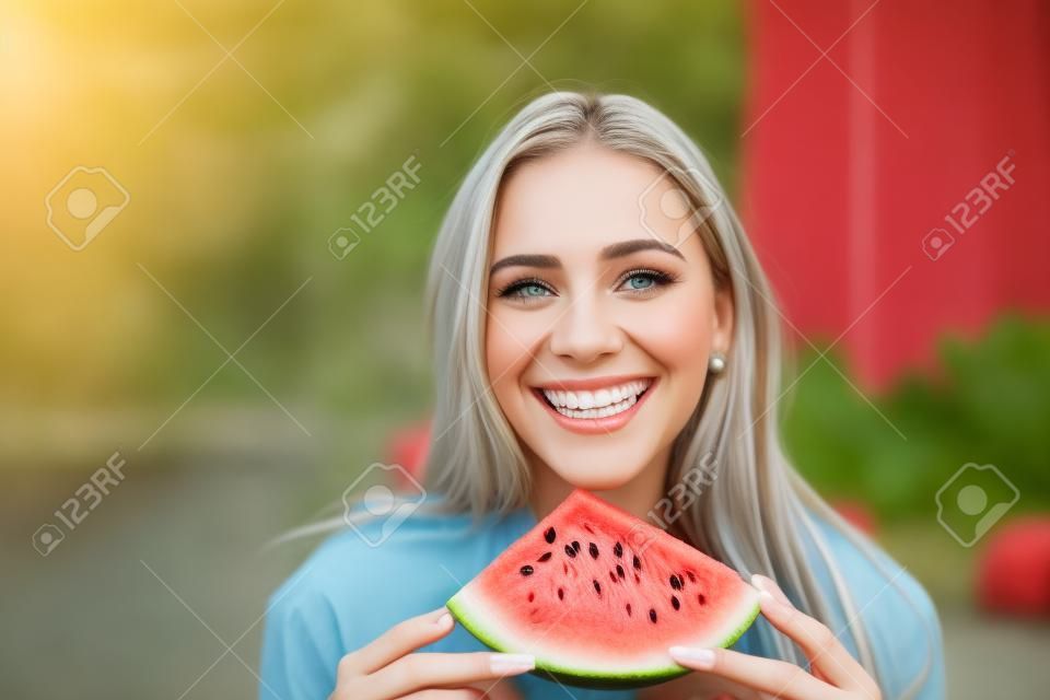 Portret pięknej młodej kobiety jedzącej arbuza i patrzącej w kamerę.