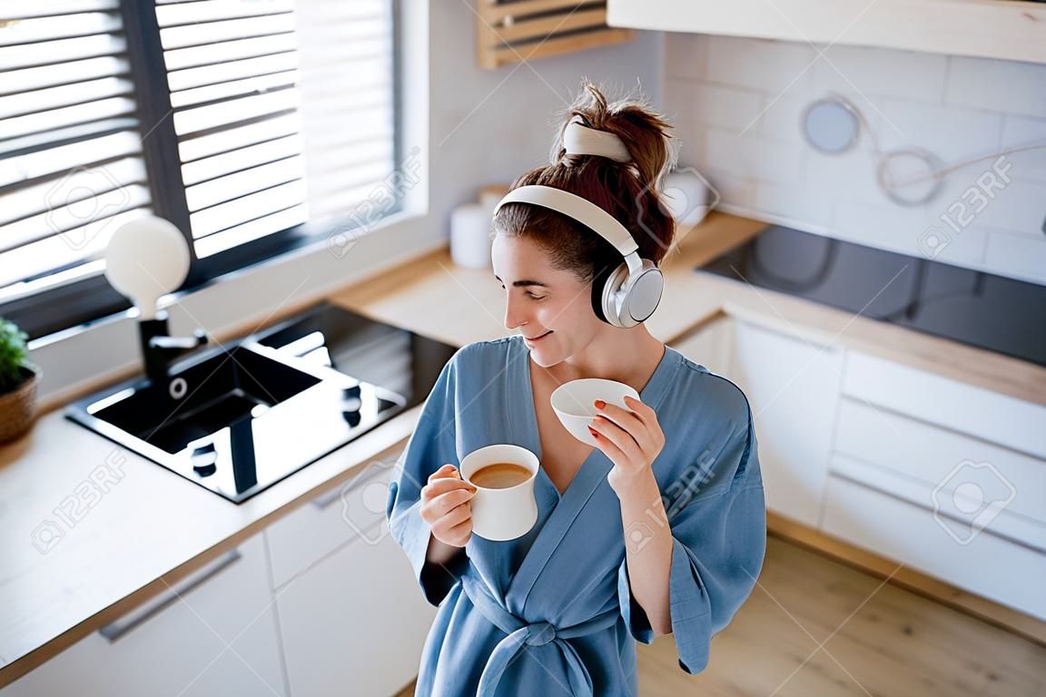 Mujer joven escuchando música y disfrutando de una taza de café por la mañana, en su cocina.